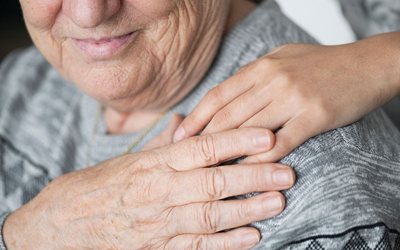 Pflegerin legt Hand auf Schulter einer älteren sitzenden Dame