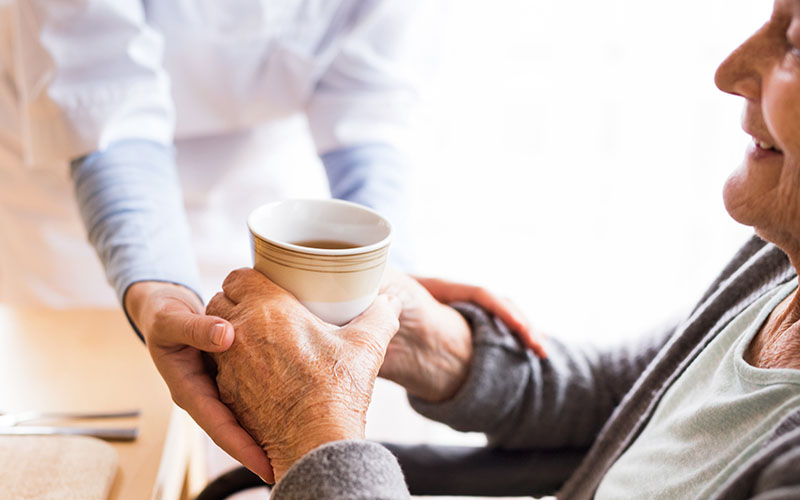 Pflegefachkraft reicht älteren Dame den Frühstückskaffee