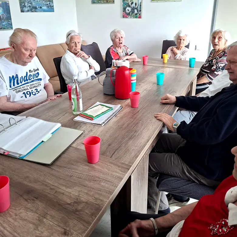 Senioren sitzen gemeinsam an großem Esstisch