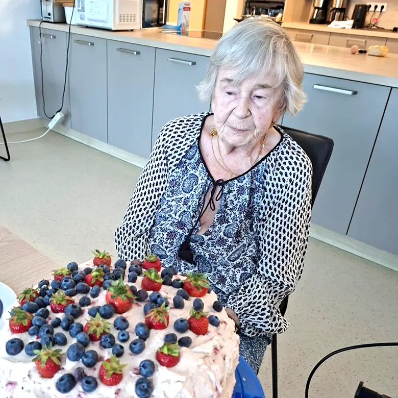 Ältere Dame betrachtet Sahnetorte, die mit frischen Beeren garniert ist