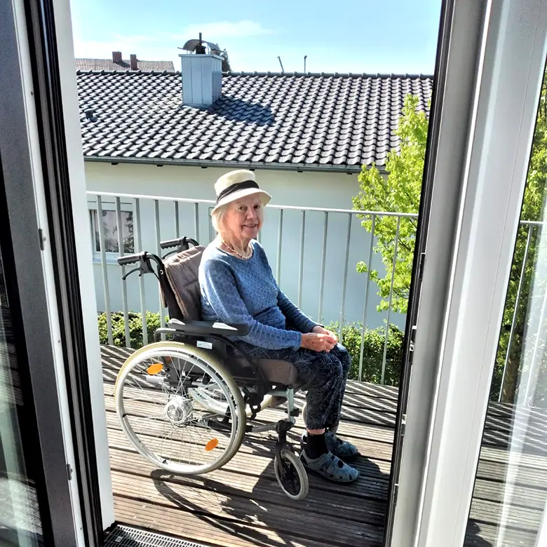 Ältere Dame mit Hut genießt Sonnenstrahlen auf ihrer Terrasse